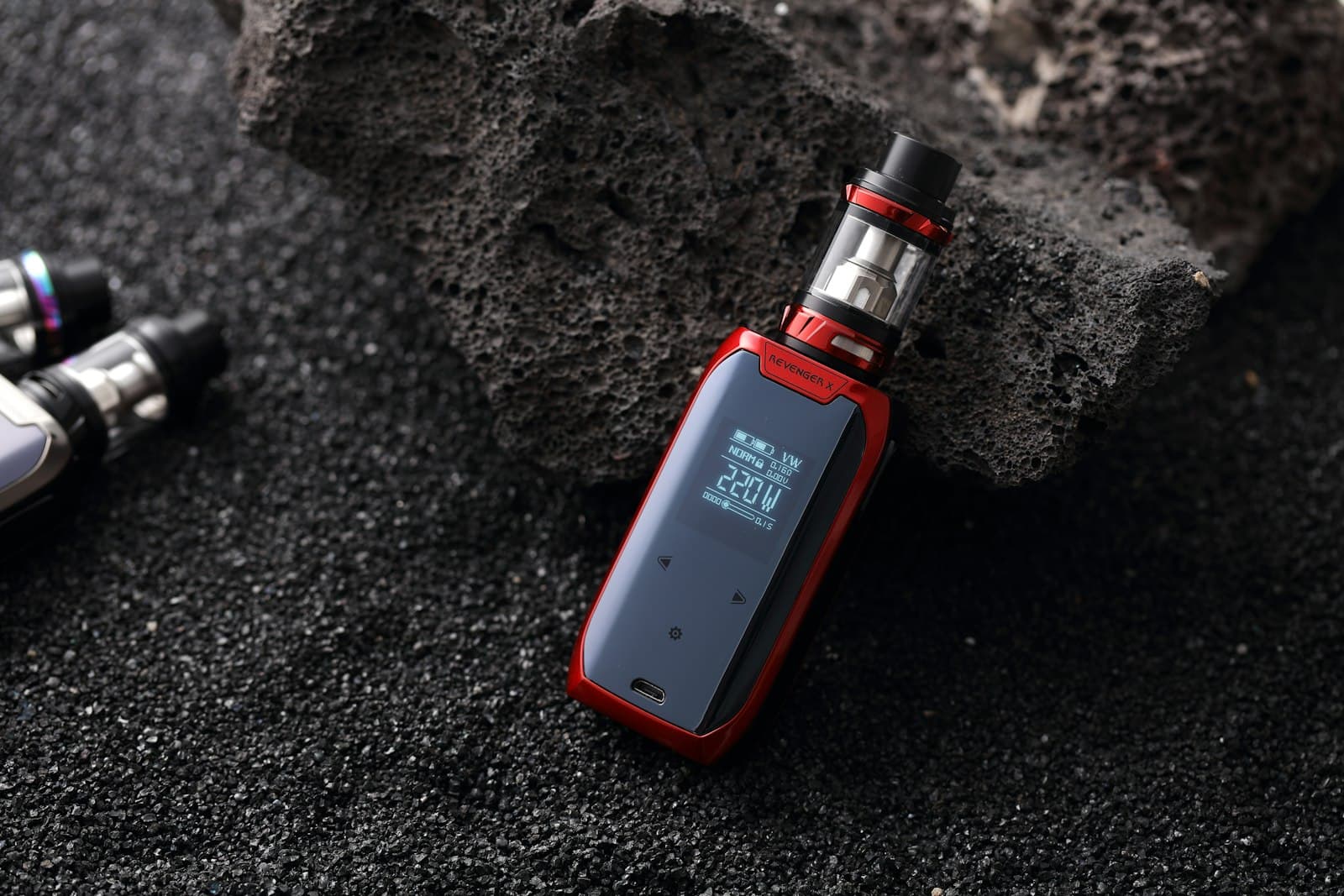 A vape mod and tank resting against a dark textured rock